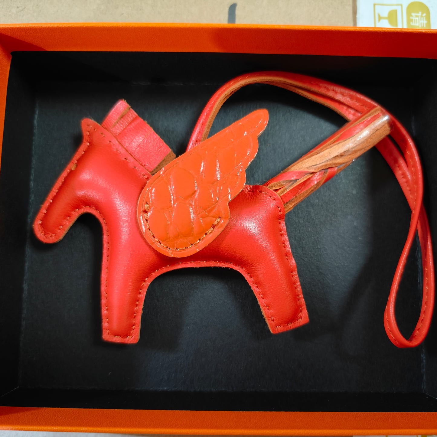 Vibrant red lambskin Pegasus charm with matching crocodile-pattern wings and leather strap in a gift box.