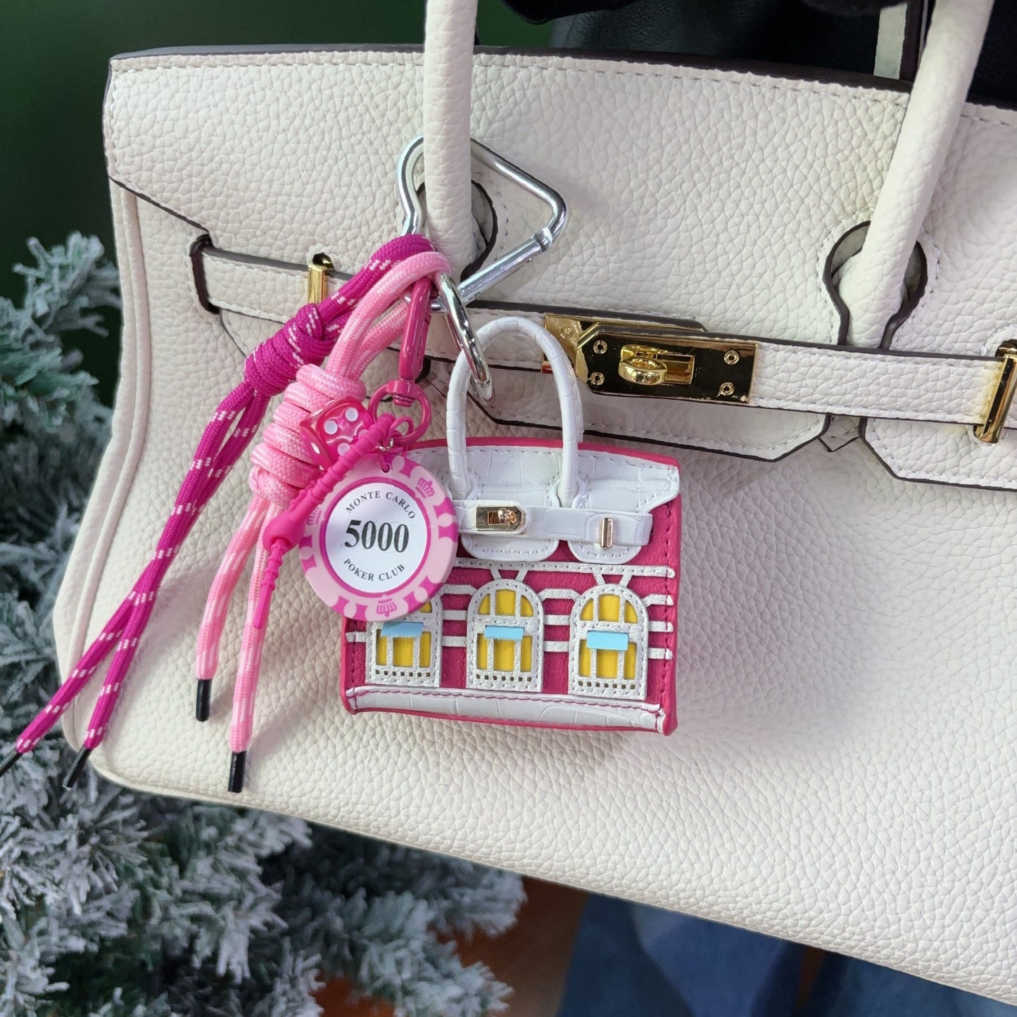 Fuchsia and white vegan leather Faubourg style mini Birk bag charm with yellow window details, used as a functional earphone case on a white pebbled leather handbag.