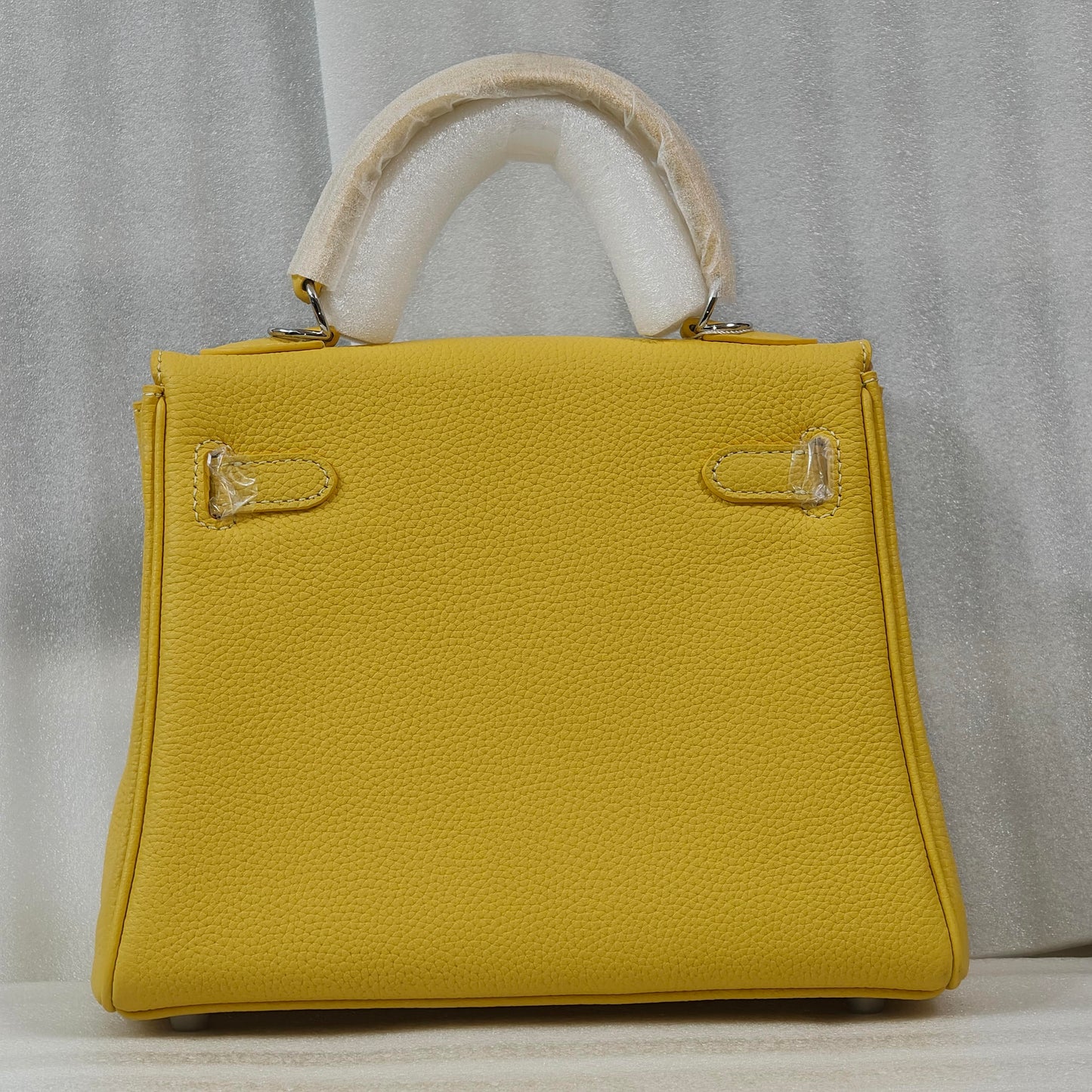 Back view of a vibrant yellow mini Kelli handbag made of premium top grain pebbled leather, featuring a sturdy top handle and gold-tone hardware.