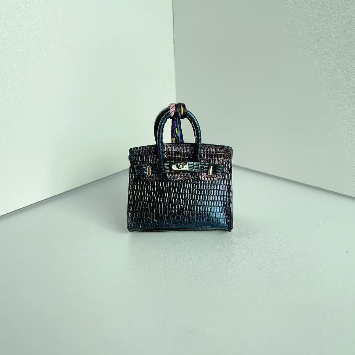 Front view of a Deep Colort mini Birkin handbag charm featuring a luxury crocodile embossed texture and silk scarf handle.