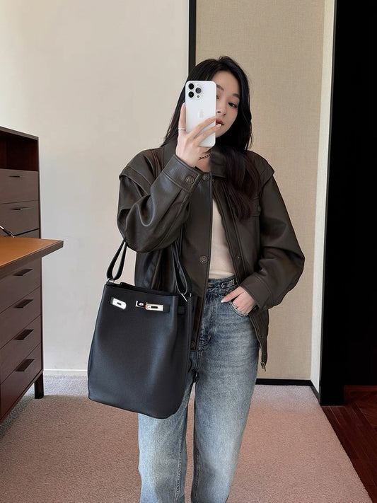Lifestyle shot of a woman carrying the black pebbled leather bucket bag as a shoulder bag, paired with a leather jacket and jeans.