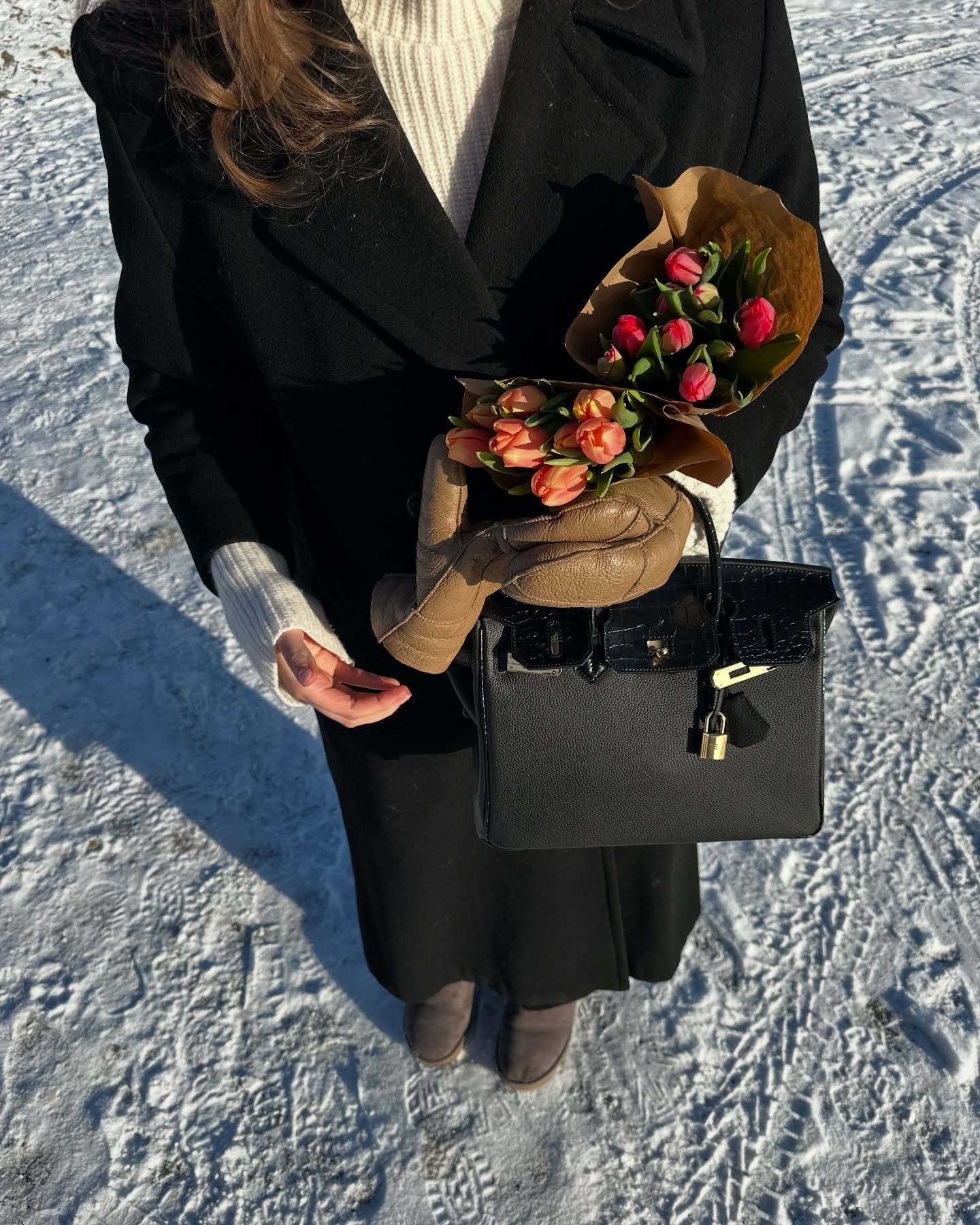 Lifestyle shot in a snowy setting featuring a black Croc Flap Berkin Bag made of Togo top grain leather, highlighting the contrast crocodile embossed flap and gold-tone hardware.