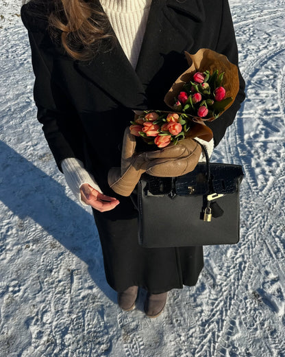Lifestyle shot in a snowy setting featuring a black Croc Flap Berkin Bag made of Togo top grain leather, highlighting the contrast crocodile embossed flap and gold-tone hardware.