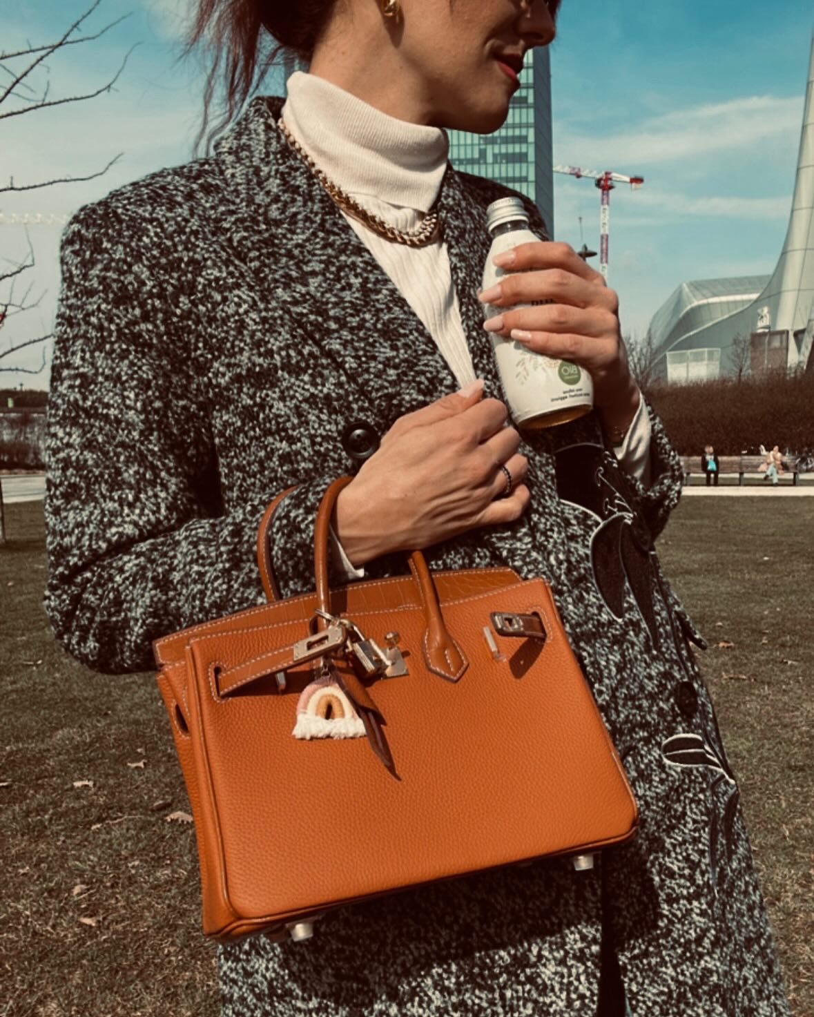 A model carrying a tan Croc Flap Berkin Bag as a handbag, styled with a tweed blazer and cream turtleneck for a sophisticated, elite lifestyle look.