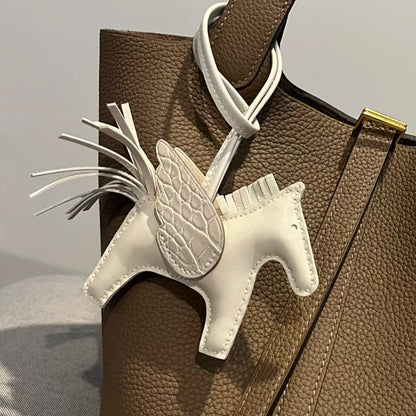 Off-white Pegasus horse charm with crocodile-pattern wings hanging on a brown leather bag.