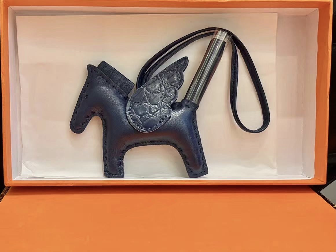 Navy blue lambskin Pegasus charm with matching crocodile-pattern wings in an orange gift box.