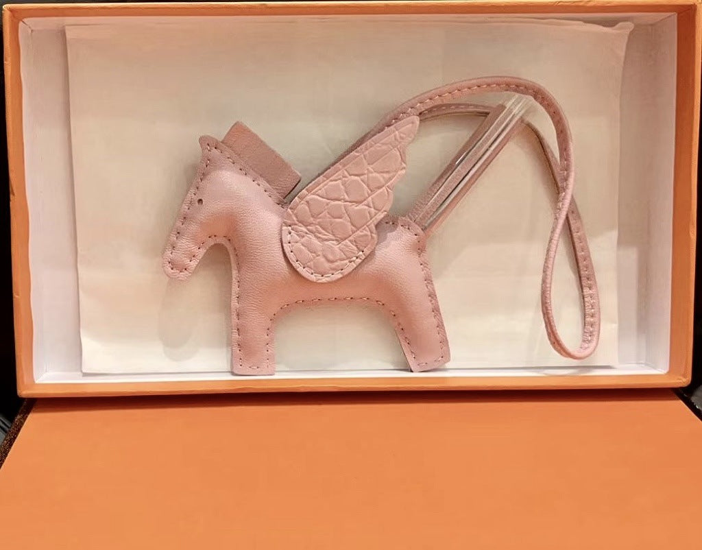 Pink lambskin Pegasus charm with crocodile-pattern wings in an orange gift box.