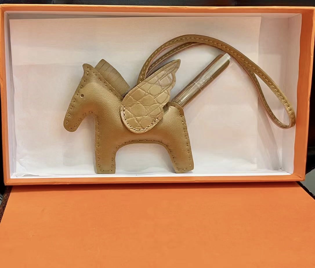 Gold lambskin Pegasus charm with matching crocodile-pattern wings in an orange gift box.