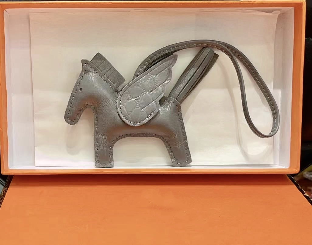Gray lambskin Pegasus charm with crocodile-pattern wings in an orange gift box.
