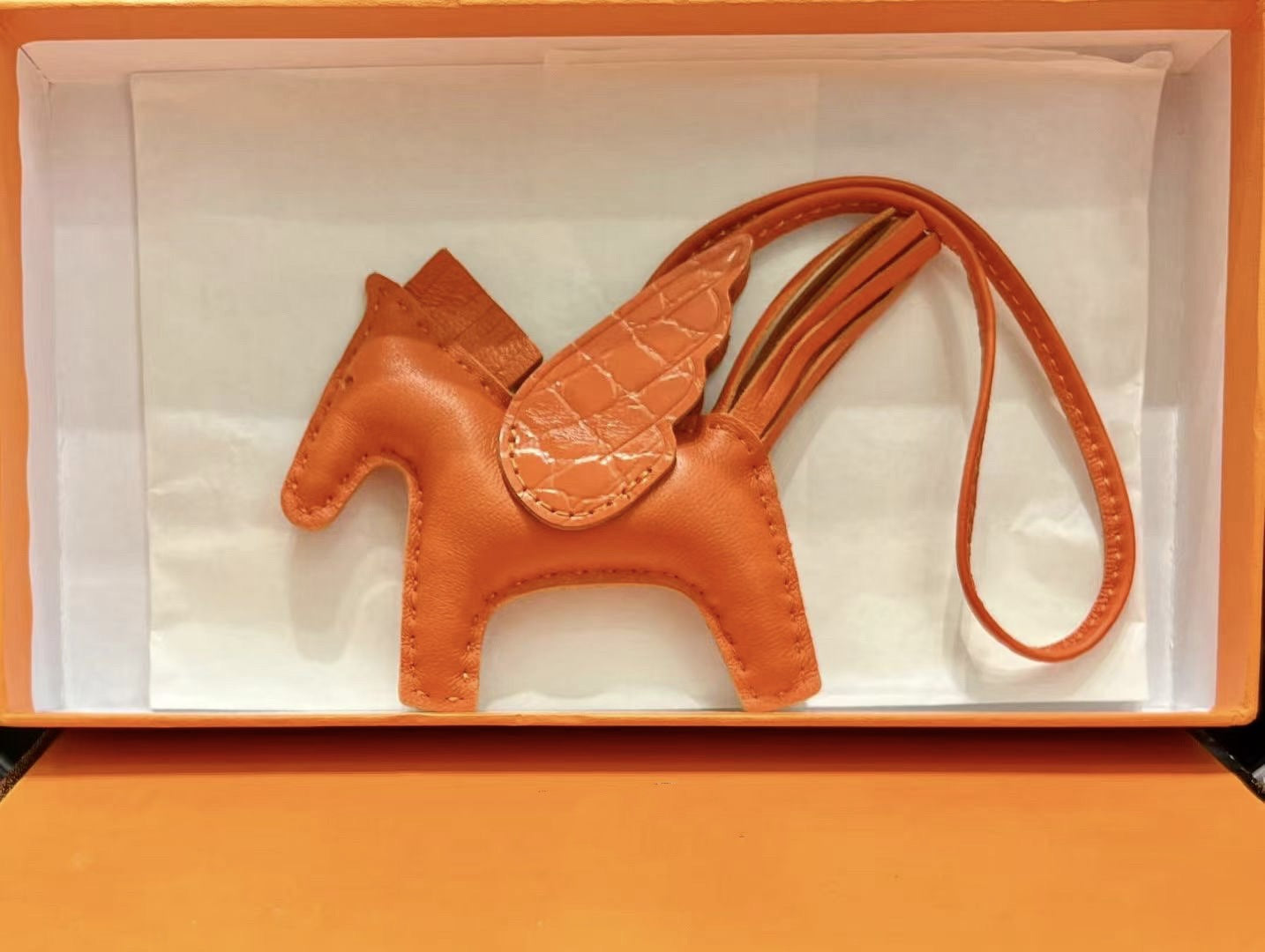 Orange lambskin Pegasus charm with crocodile-pattern wings in an orange gift box.
