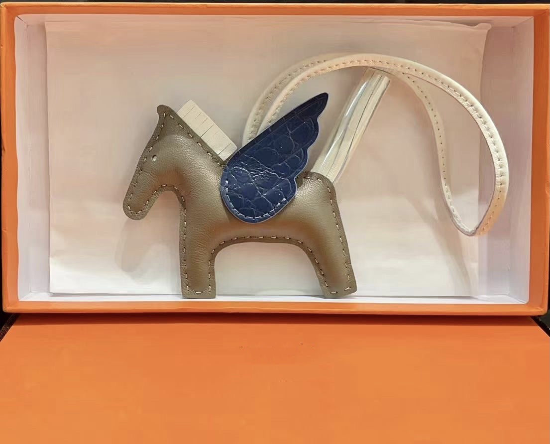 Tricolor Pegasus charm with gray body, navy blue crocodile-pattern wings, and white strap in a gift box.