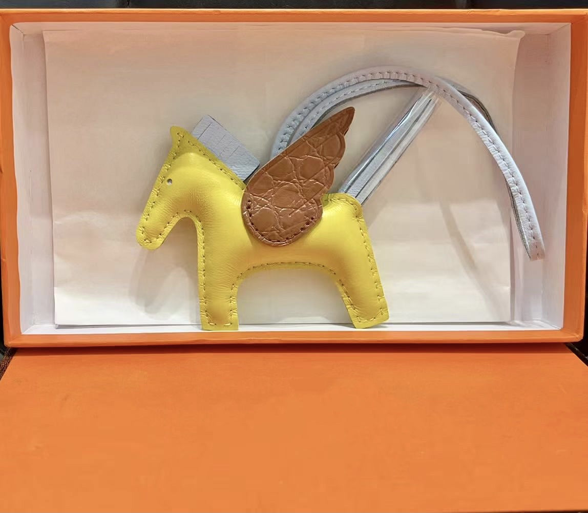 Tricolor Pegasus charm with off-white body, pink strap, and brown crocodile-pattern wings in an orange gift box.