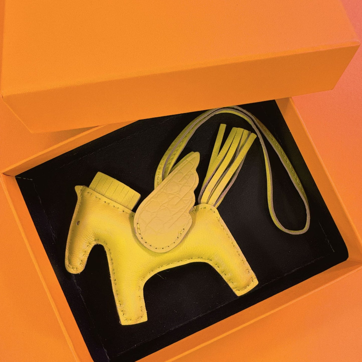 Yellow lambskin Pegasus charm with beige crocodile-pattern wings in an orange gift box.