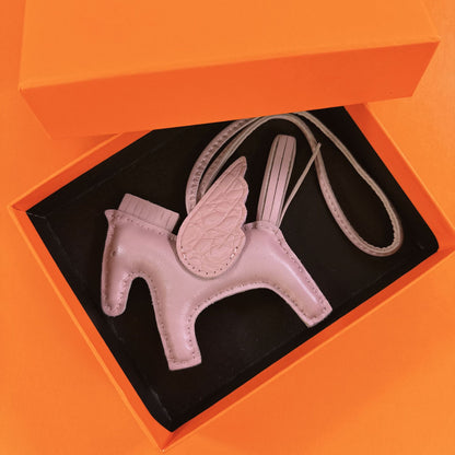 Light pink lambskin Pegasus charm with matching crocodile-pattern wings in an orange gift box.