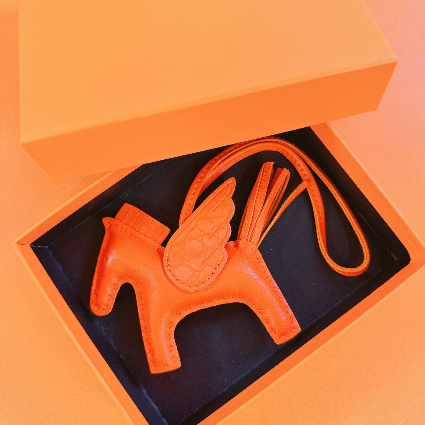 Bright orange lambskin Pegasus charm with matching crocodile-pattern wings in an orange gift box.