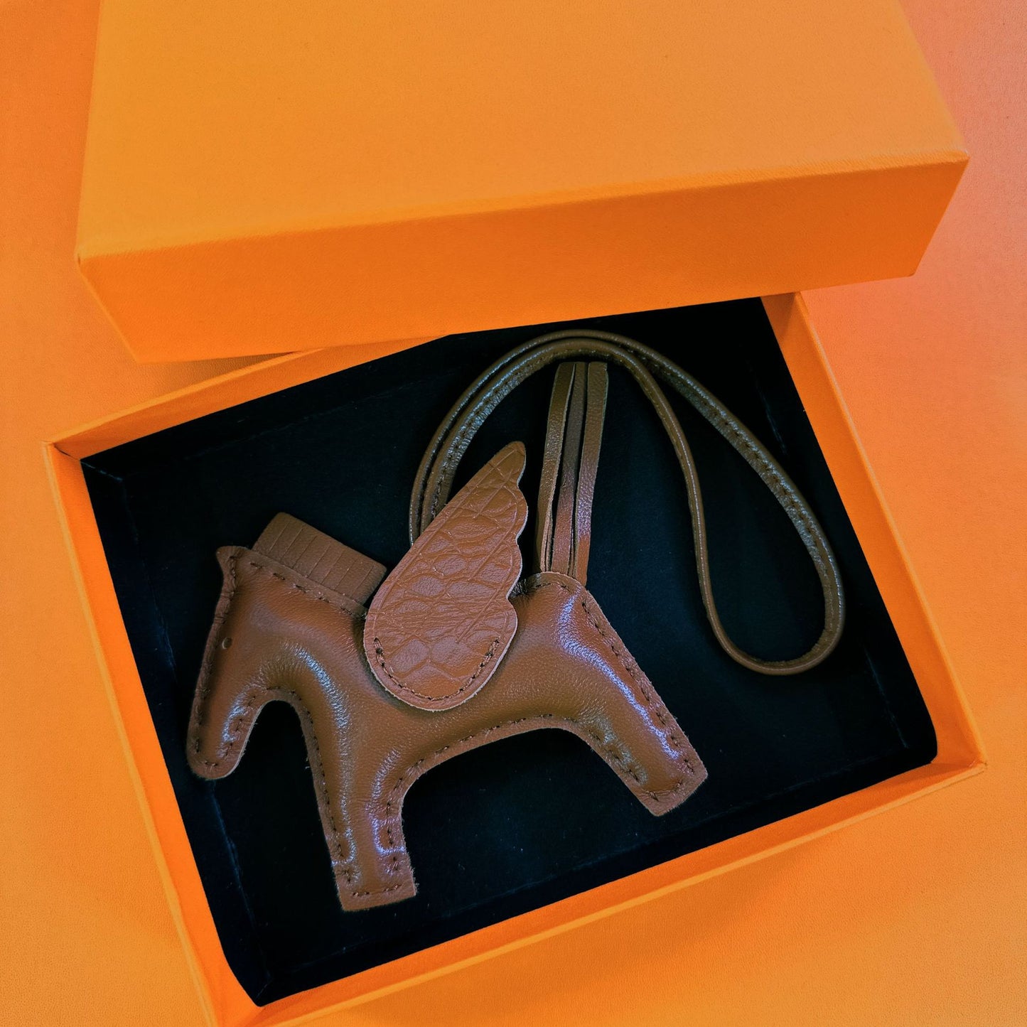 Brown lambskin Pegasus charm with matching crocodile-pattern wings in an orange gift box.