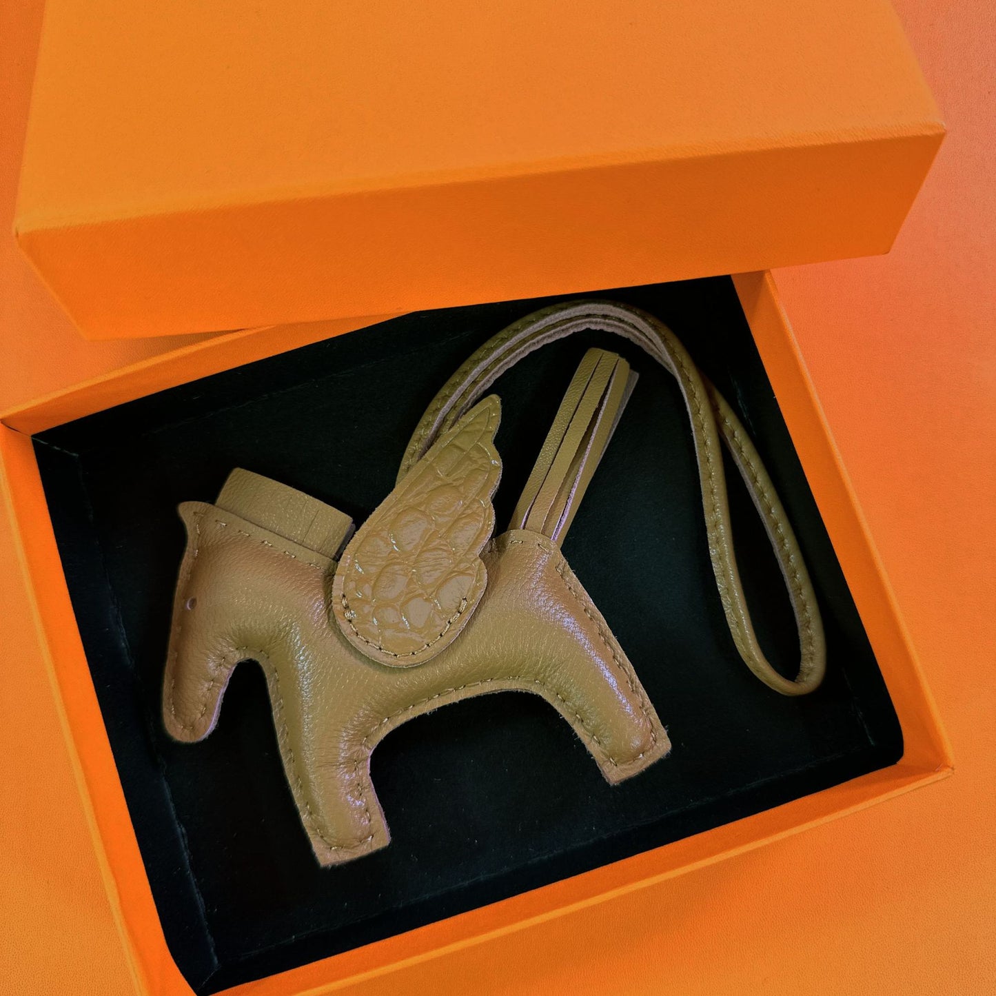 Olive green lambskin Pegasus charm with matching crocodile-pattern wings in an orange gift box.