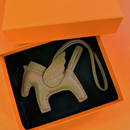 Olive green lambskin Pegasus charm with matching crocodile-pattern wings in an orange gift box.