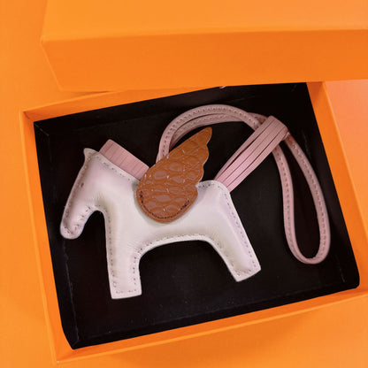 Tricolor Pegasus charm with white body, brown crocodile-pattern wings, and pink strap in a gift box.