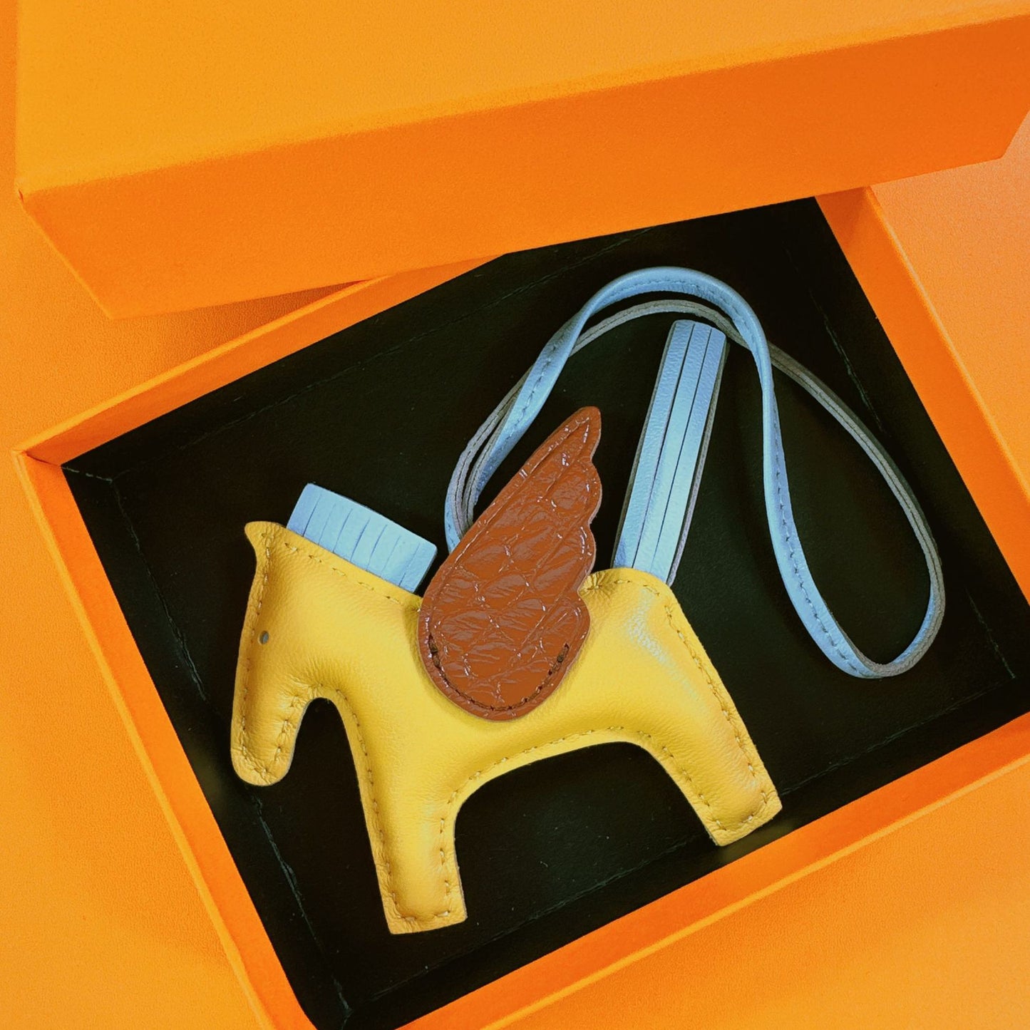 Tricolor Pegasus charm with yellow body, light blue strap, and brown crocodile-pattern wings in a gift box.
