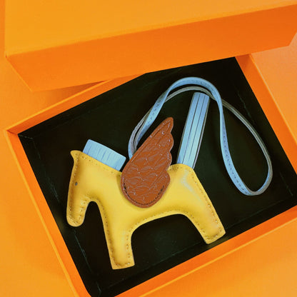 Tricolor Pegasus charm with yellow body, light blue strap, and brown crocodile-pattern wings in a gift box.