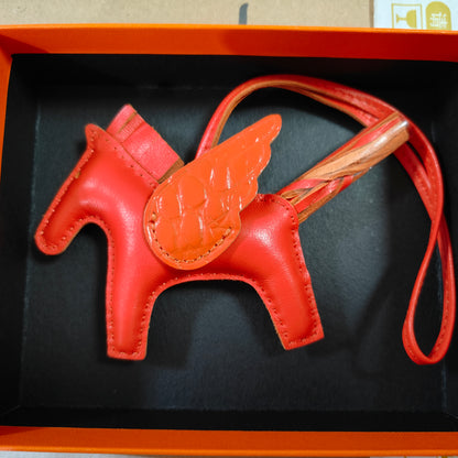 Vibrant red lambskin Pegasus charm with matching crocodile-pattern wings and leather strap in a gift box.