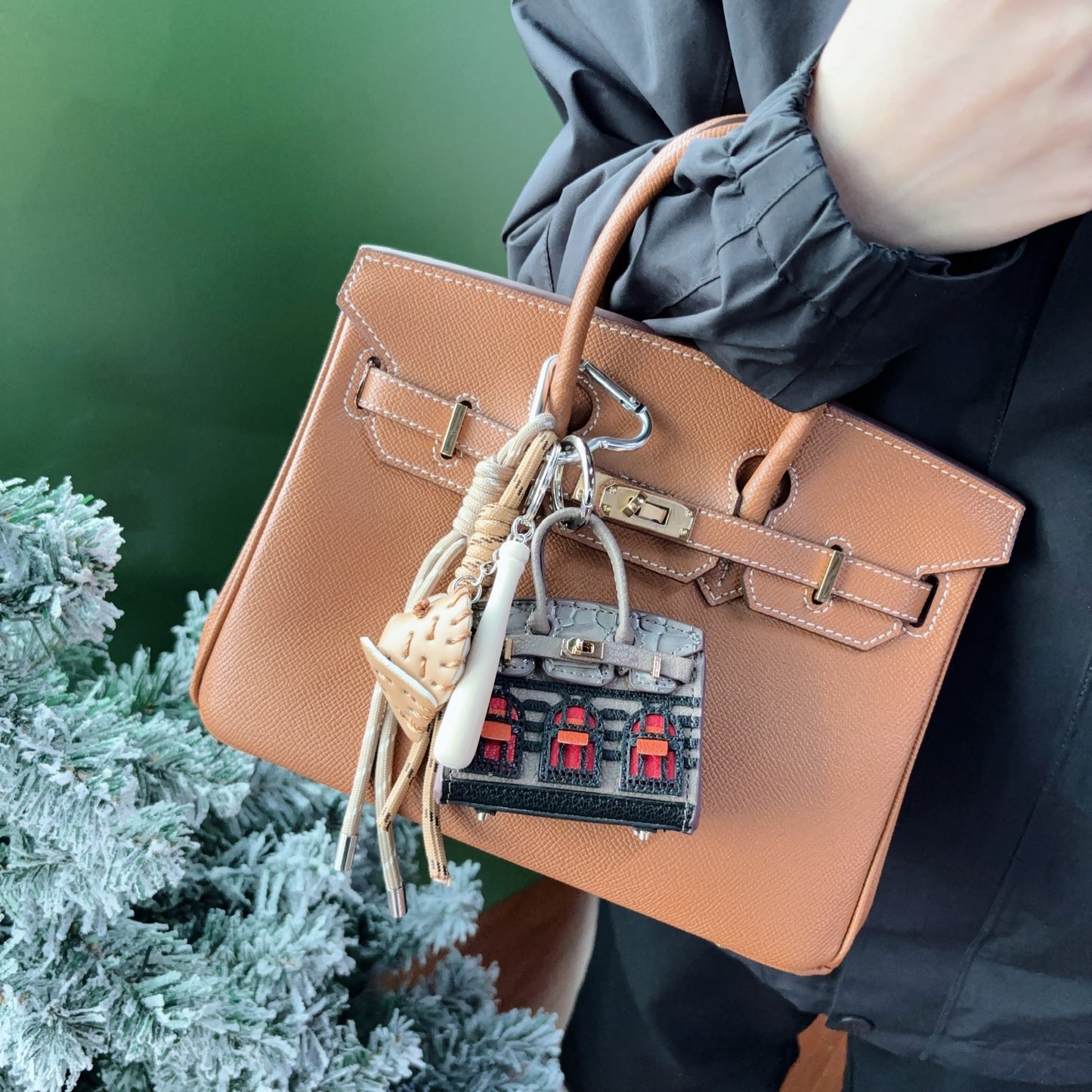 A dark grey vegan leather Faubourg style mini Birk bag charm with vibrant red window details, used as a stylish earphone storage bag on a tan handbag.