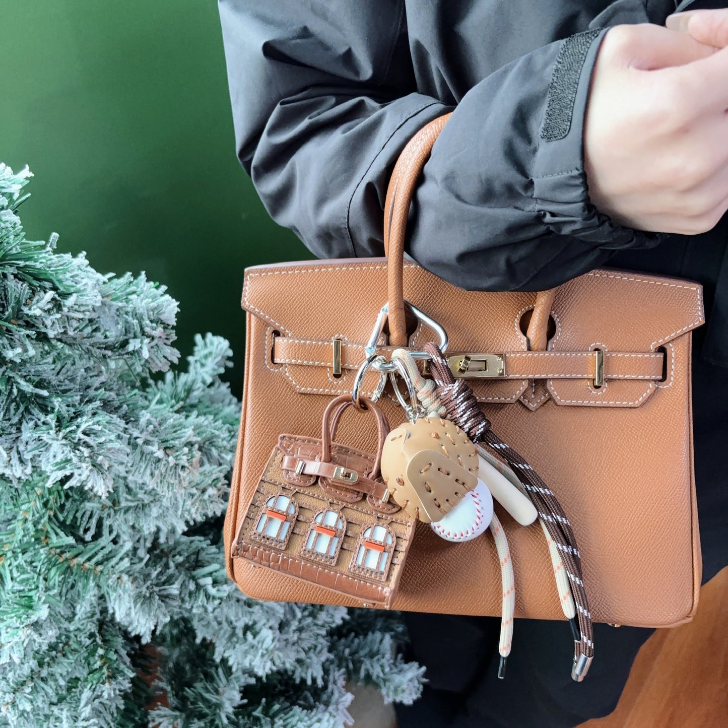 A taupe vegan leather Faubourg style mini Birk bag charm with orange window accents, functioning as an earphone storage bag on a classic tan leather handbag.
