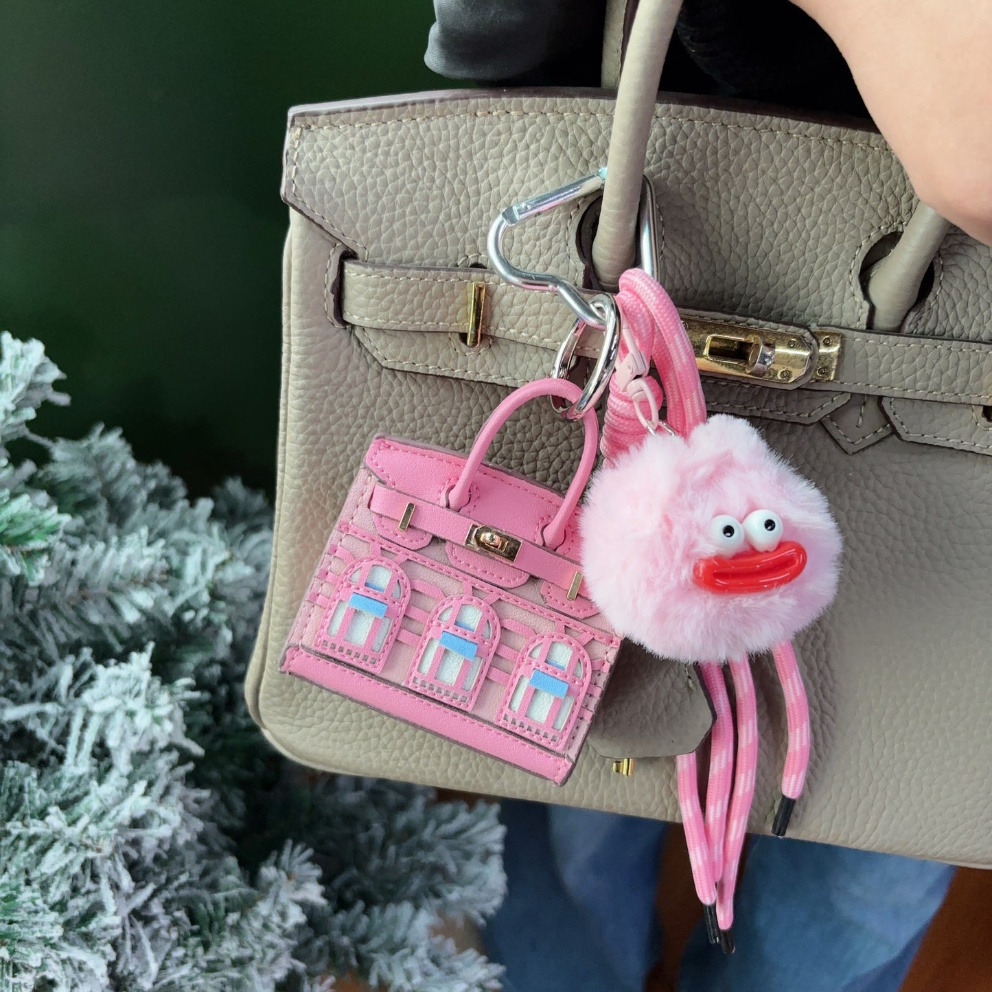 Pink vegan leather Faubourg style mini Birk bag charm with light blue window details, used as an earphone storage case on a grey leather handbag.