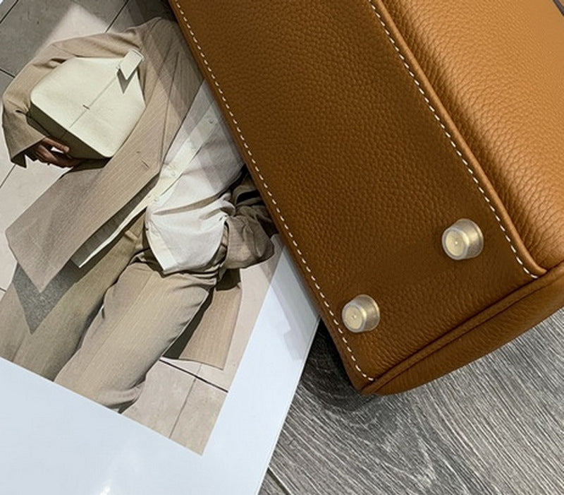 The base of a tan mini Kelli bag featuring protective metal feet and precise white stitching on top grain pebbled leather.