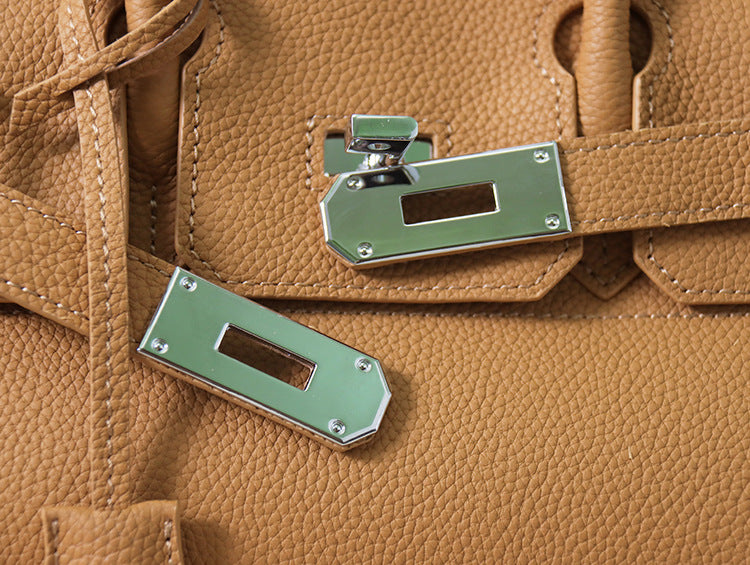 Close-up of a tan JPG Birkin inspired handbag, showcasing the textured top grain cowhide leather and polished silver-tone lock closure hardware.