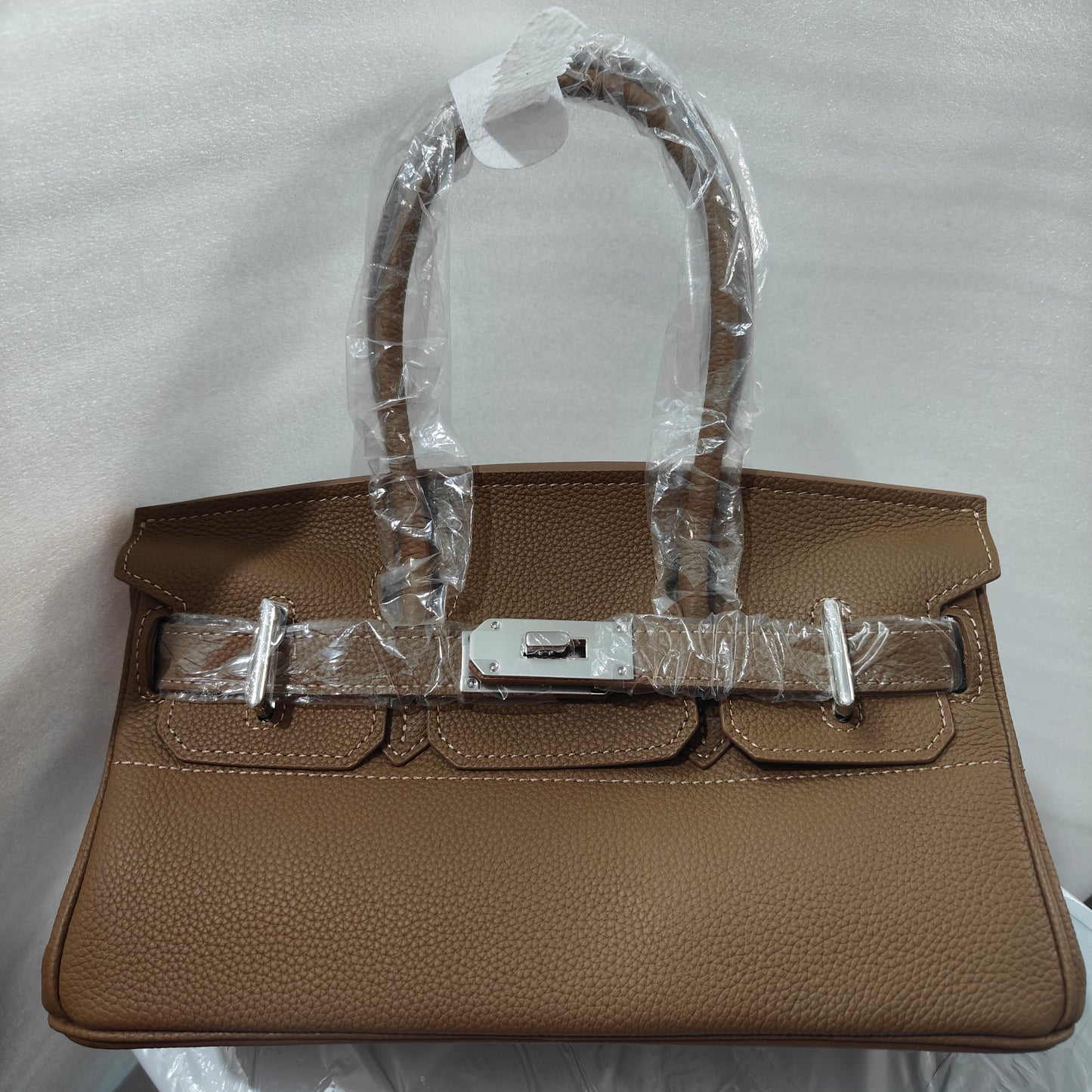 Front view of a Khaki JPG Birkin inspired handbag in textured top grain cowhide leather, featuring silver-tone lock closure hardware and a matching clochette.