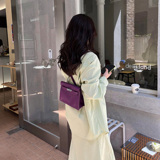 A woman styling a purple top grain leather Kelli Danse bag as a chic backpack, paired with a pale yellow outfit for a sophisticated street-style look.