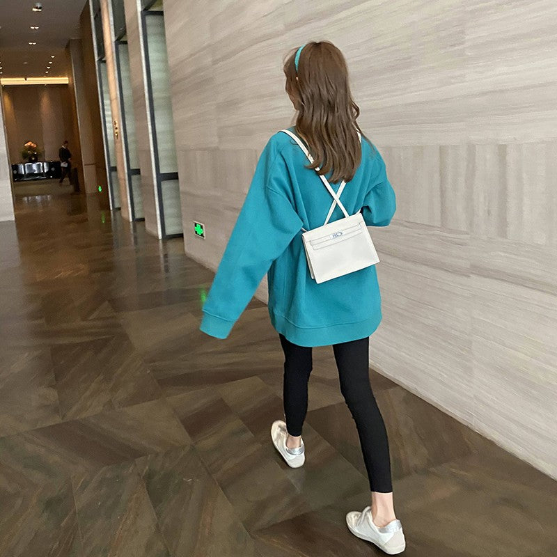 A woman styling a Milkshake White top grain leather Kelli Danse bag as a backpack with a turquoise sweatshirt for a fresh, casual look.