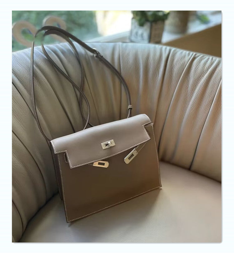 An Etoupe taupe leather Kelli Danse shoulder bag with silver hardware and a long adjustable strap, resting on a beige leather armchair.