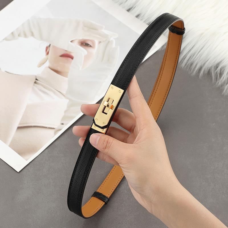 Holding a black Epsom leather Kelli belt, featuring a polished gold turn-lock clasp and a tan lining.
