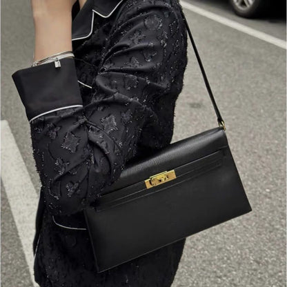 Model wearing black Epsom leather inspired Kelly Elan shoulder bag with gold hardware on street.