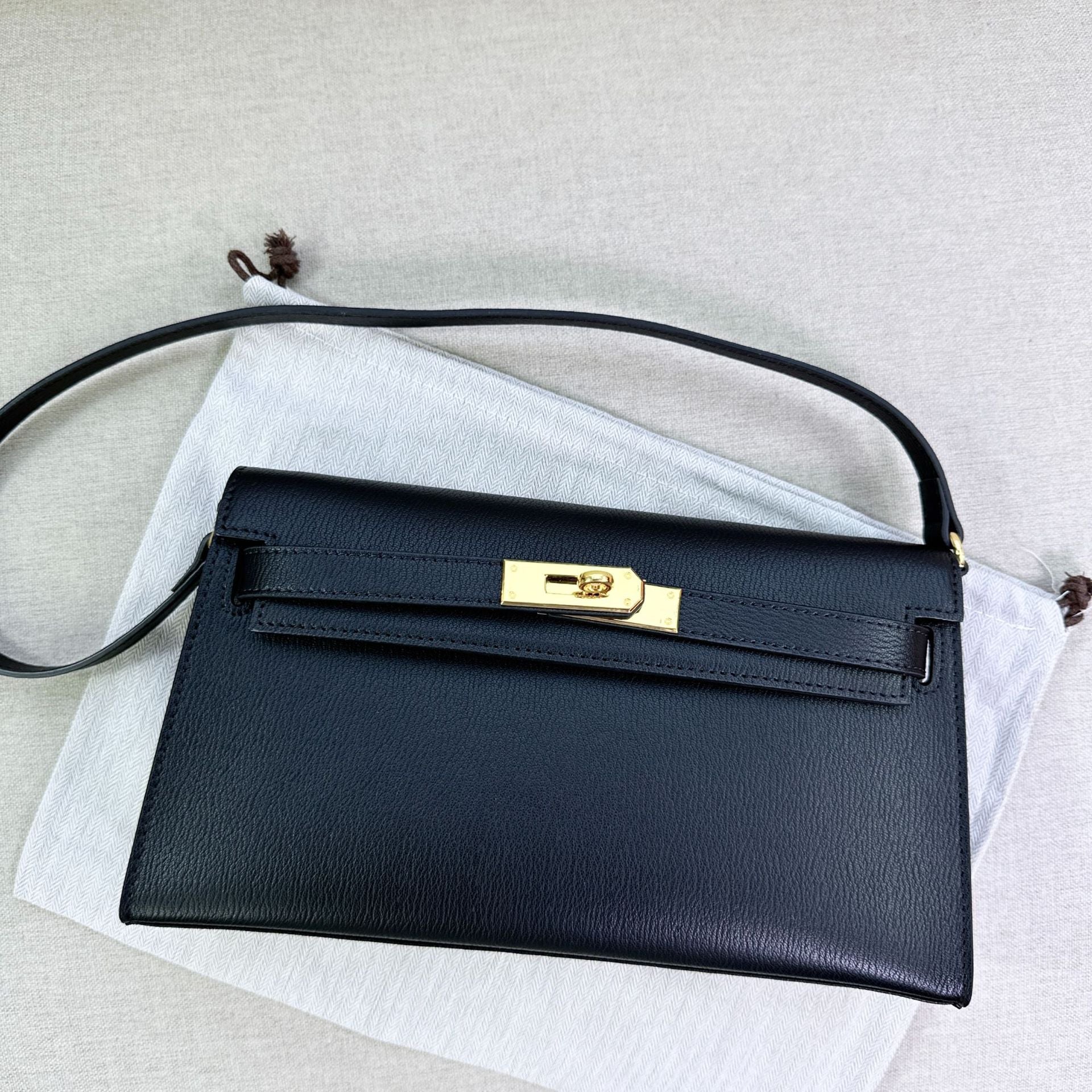 Black split leather inspired Kelly Elan shoulder bag with gold hardware and shoulder strap on a white dust bag.