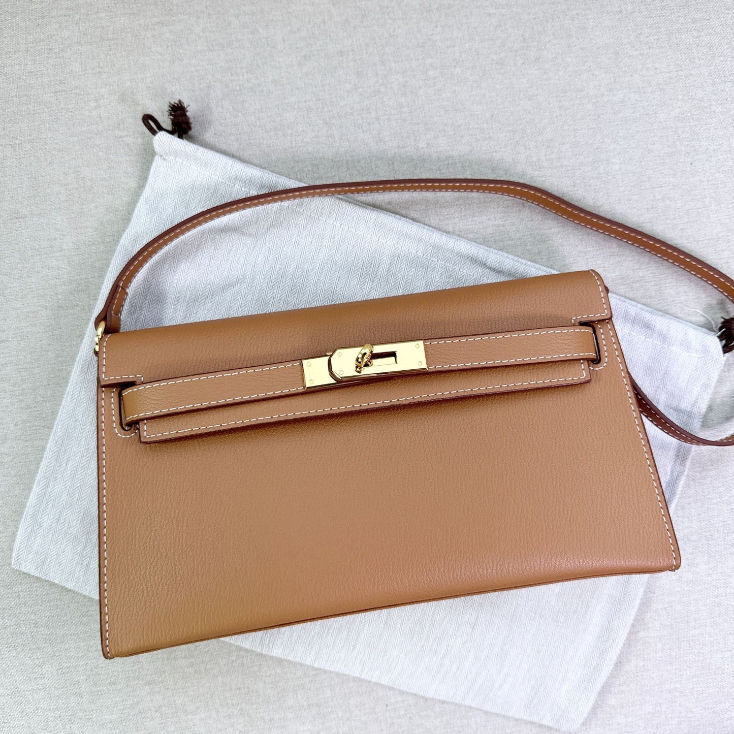 Gold brown split leather inspired Kelly Elan shoulder bag with gold hardware and shoulder strap on a white dust bag.