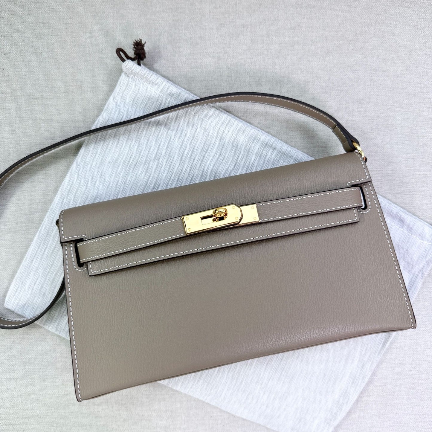 Gray split leather inspired Kelly Elan shoulder bag with gold hardware and shoulder strap on a white dust bag.