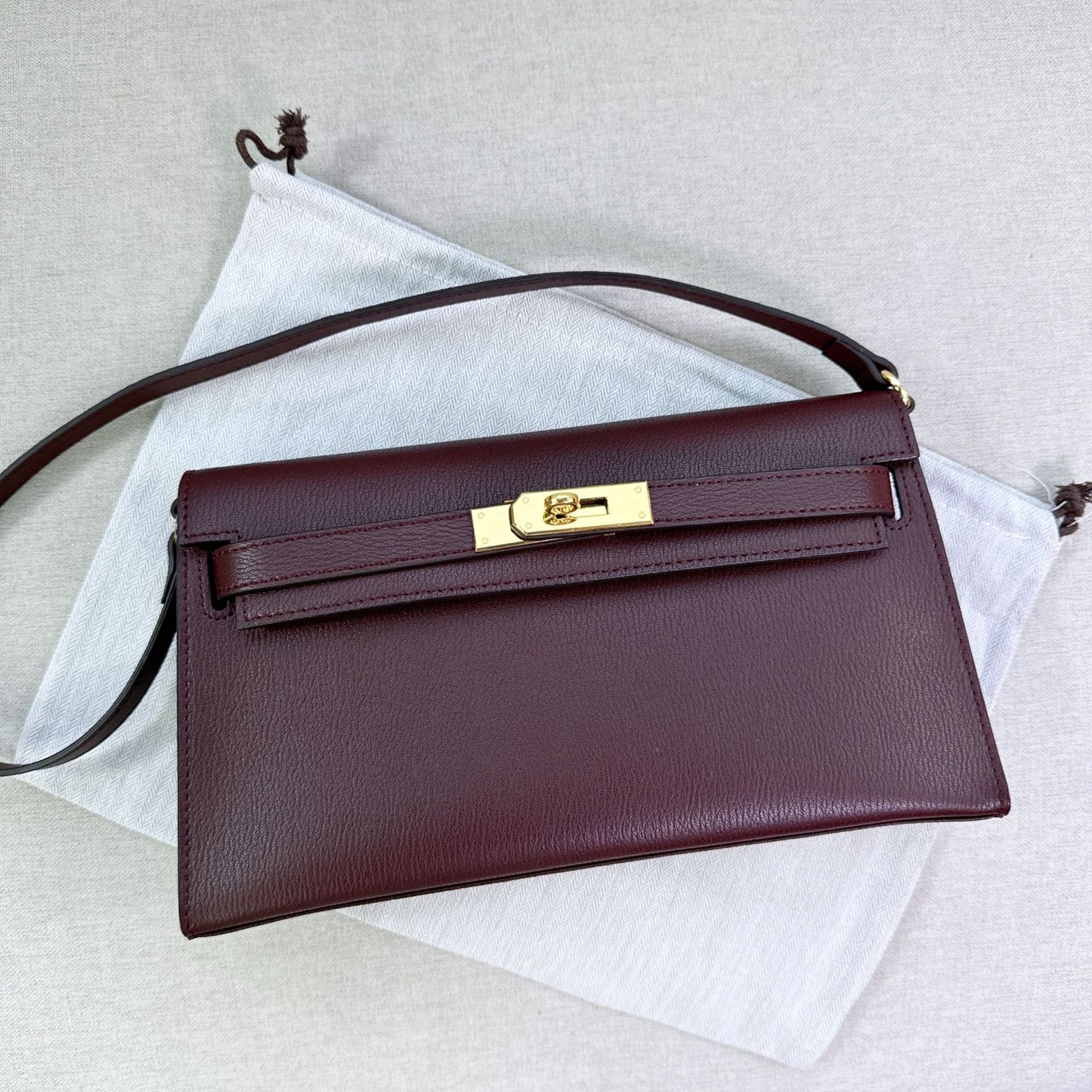 Wine split leather inspired Kelly Elan shoulder bag with golden hardware on a white dust bag.