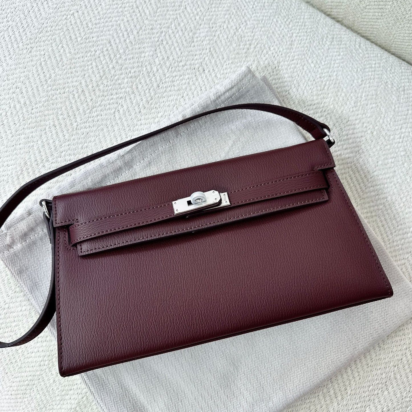Wine red split leather inspired Kelly Elan shoulder bag with silver hardware on a white dust bag.