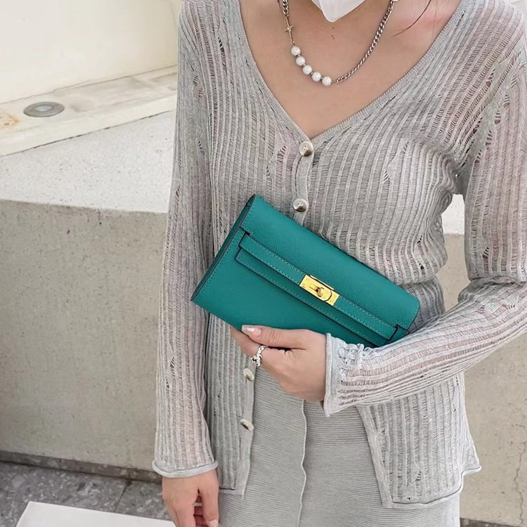 A model holding a vibrant Lake Green inspired Kelly to go wallet as a chic clutch, styled with a grey ribbed cardigan for a sophisticated and modern everyday look.
