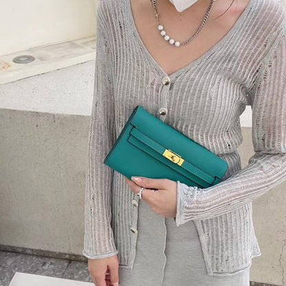 A model holding a vibrant Lake Green inspired Kelly to go wallet as a chic clutch, styled with a grey ribbed cardigan for a sophisticated and modern everyday look.