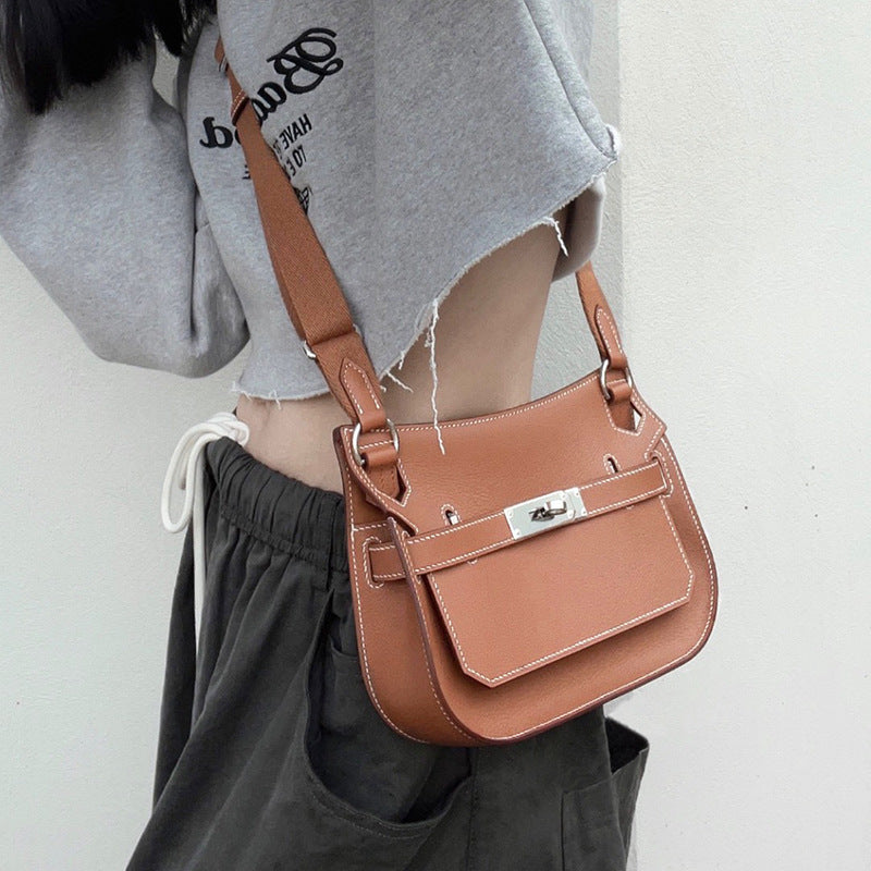 A Golden Brown leather Gypsy crossbody bag with white stitching, styled with a grey cropped sweatshirt and cargo pants for a modern casual look.