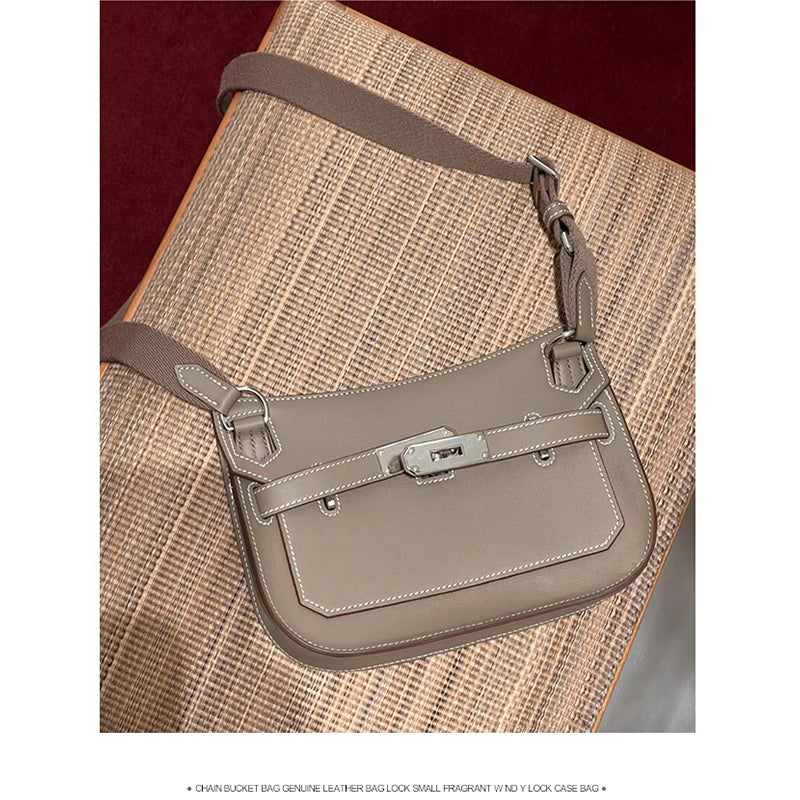A Taupe leather Gypsy shoulder bag with white contrast stitching and silver-tone hardware, resting on a textured woven surface.