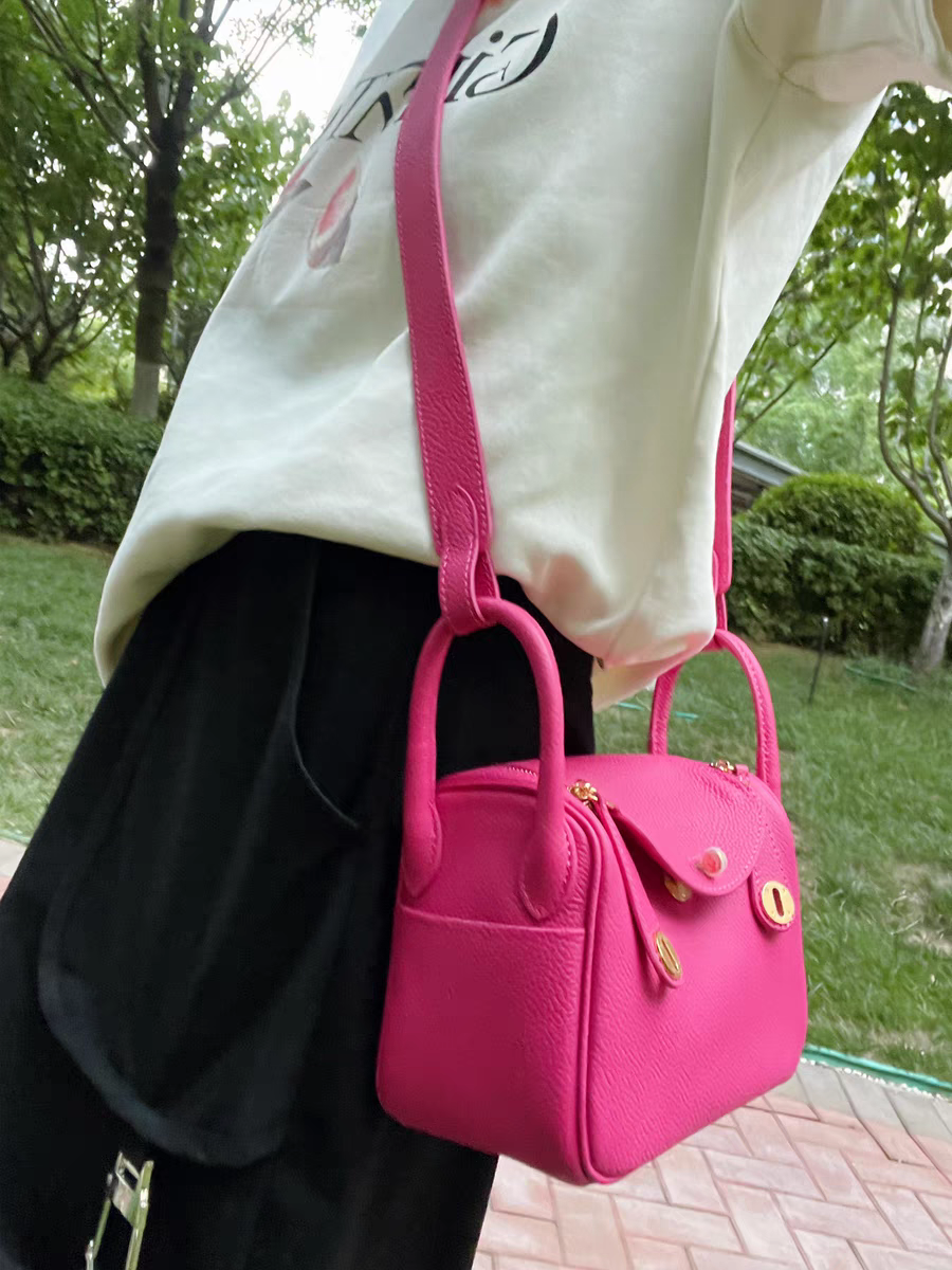 Model wearing a raspberry red top grain leather Lindy bag as a shoulder bag