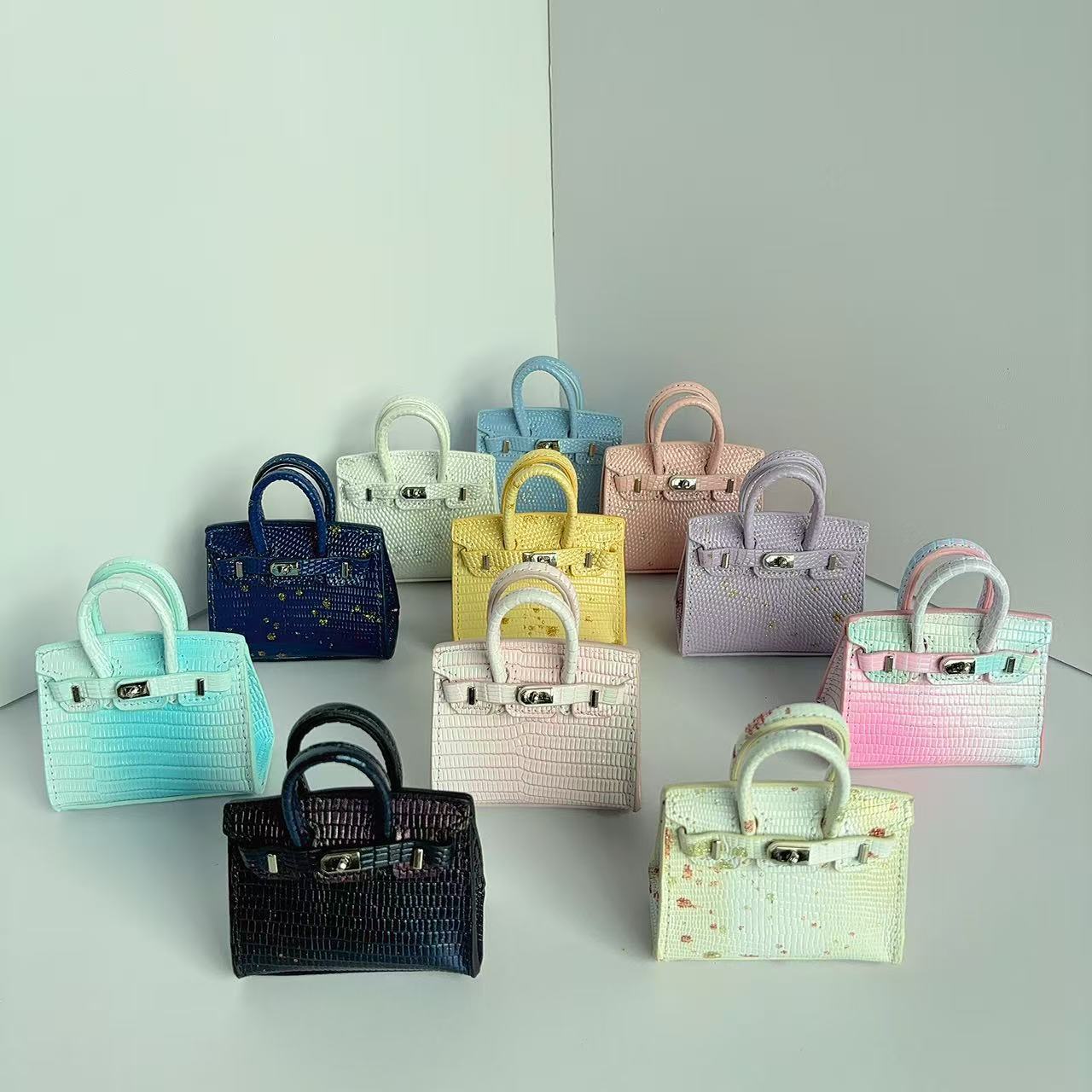 A collection of mini Birkin handbag charms in various colors and leather textures, including gradient crocodile and ostrich patterns, used as earphone cases.