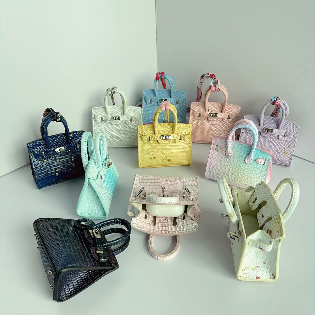 A variety of colorful mini Burkin handbag charms in gradient and crocodile textures, showing both exterior details and open interior.