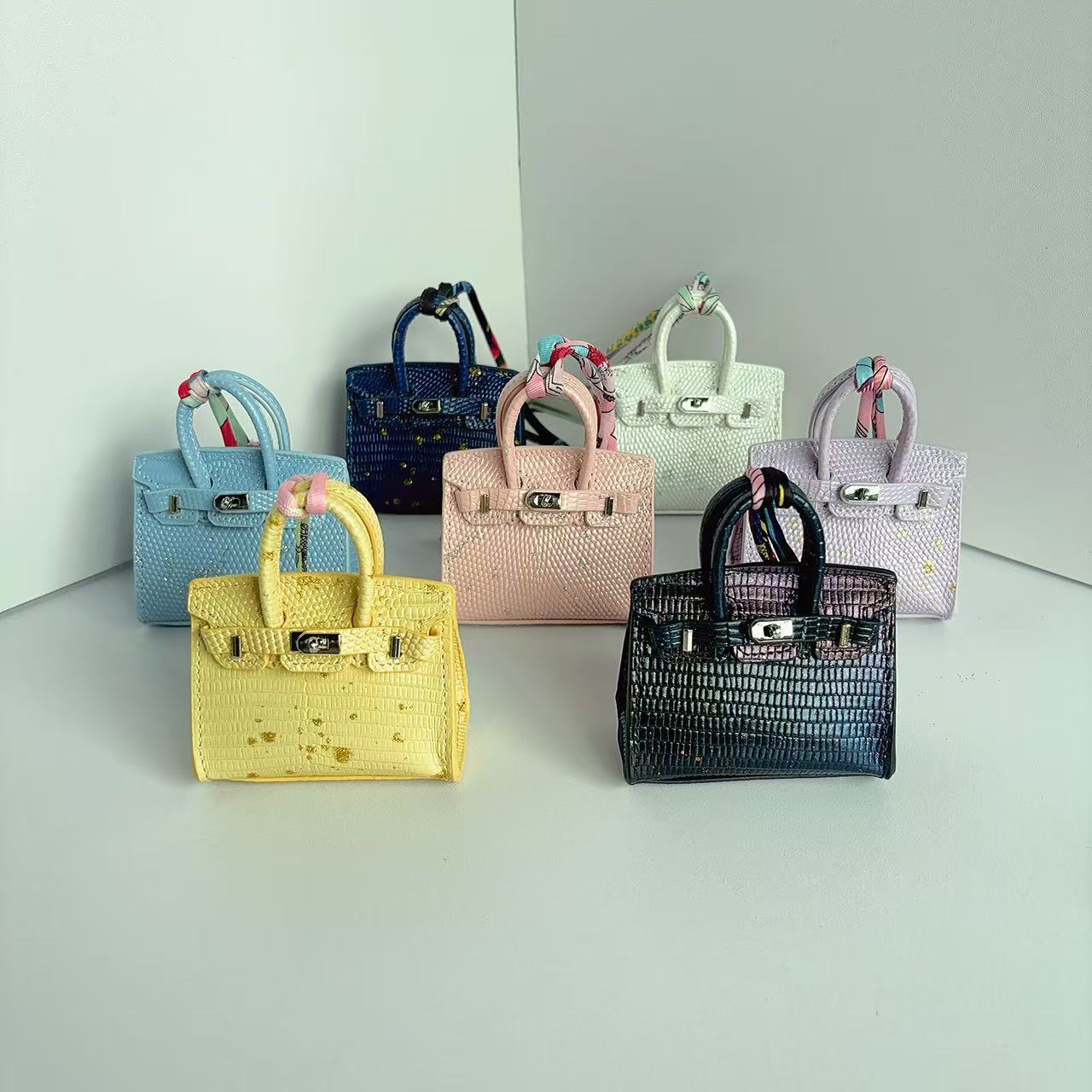 A collection of mini Birkin handbag charms in vibrant colors with various embossed leather textures and colorful silk scarf details.
